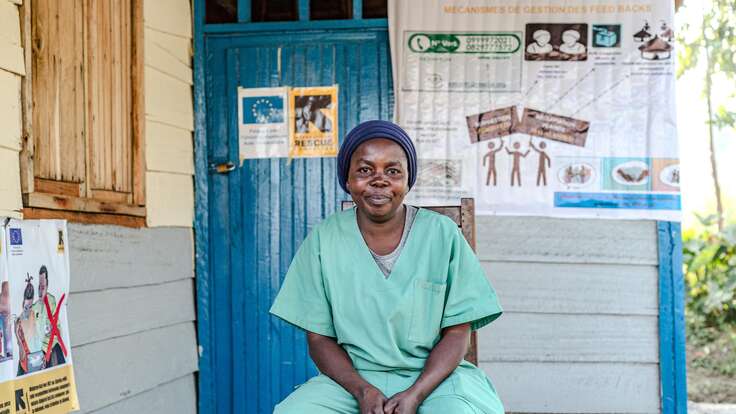 Neema; a midwife, seated in her scrubs. 