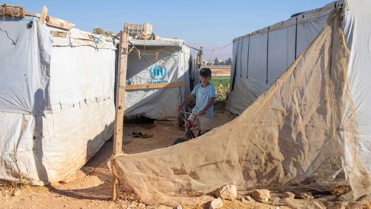 Osama fährt mit einem Fahrrad zwischen den Zelten umher.