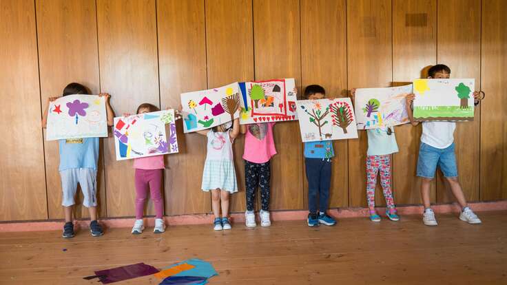 Children holding up their drawing over their faces