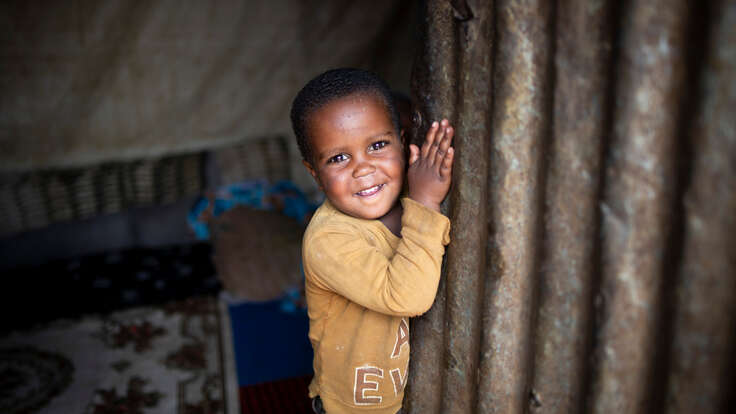 Kindesa (3) lächelt, als er die Tür seines Zuhauses im Geflüchtetenlager für Binnenvertriebene in Deder, Äthiopien, öffnet.
