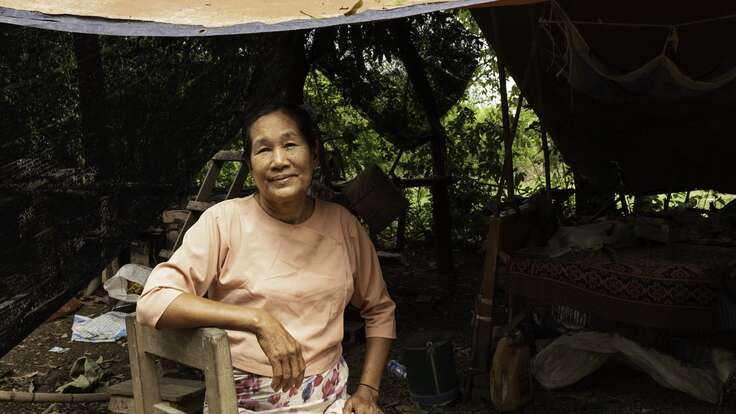 한 여성이 텐트 아래 앉아서 카메라를 바라보고 있습니다.