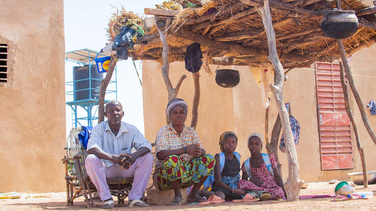 Bila Natama sitzt mit ihren Töchtern und ihrem Mann unter einem Unterstand vor ihrem Grundstück in Tibga, Burkina Faso 
