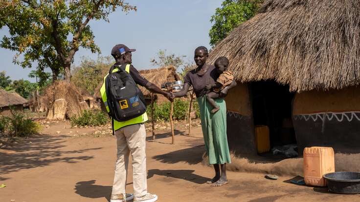 Martin greets Elizabeth, who is holding her young child during a home visit. For many families in the settlement, a knock at the door from Martin is the first step toward getting care.