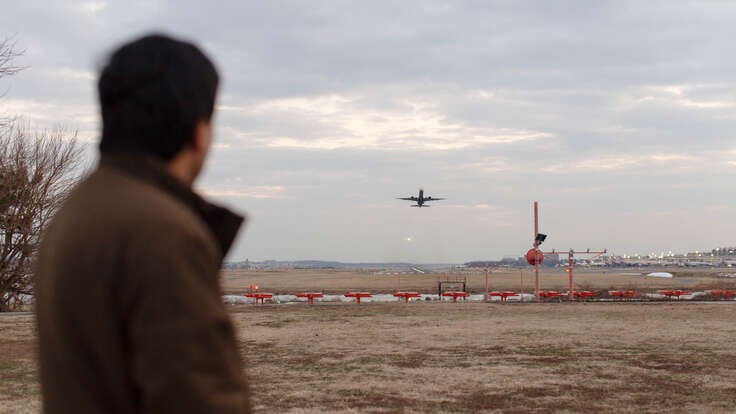 A man looks on as a plane takes off at an airport.