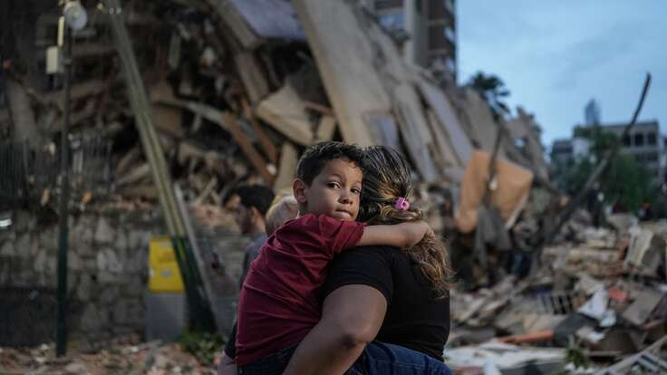 A person carries a child in front of a pile of rubble and destroyed buildings after an earthquake in Venezuela.