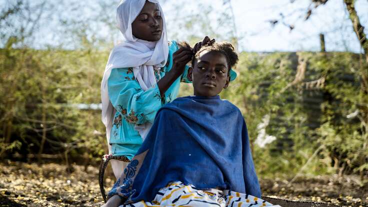 Aisha, 13, braids her friend’s hair outside her home in Aburakham village, Gadaref State, Sudan.
