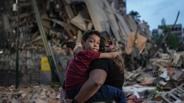 A person carries a child in front of a pile of rubble and destroyed buildings after an earthquake in Venezuela.