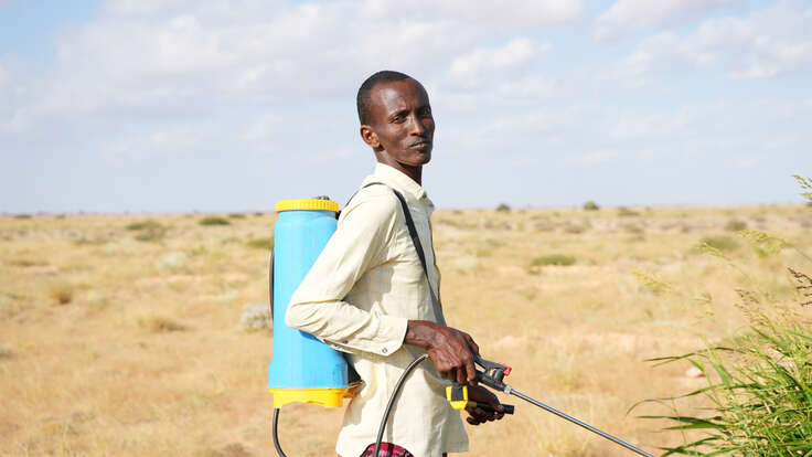 Man standing with pesticide spray in front of arid landscape