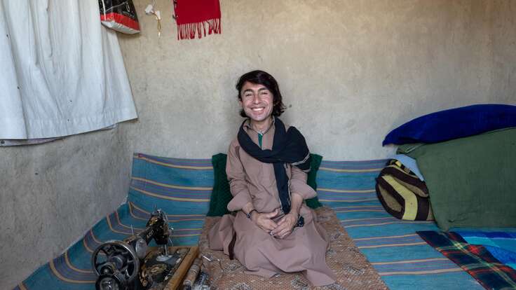Darweza sits smiling at home beside his sewing machine.