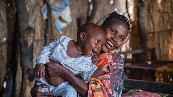 A mother holds her young child close as the two share a smile while playing.