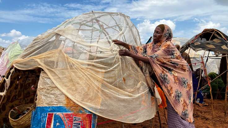 A woman works on improving her makeshift shelter in Somalia.