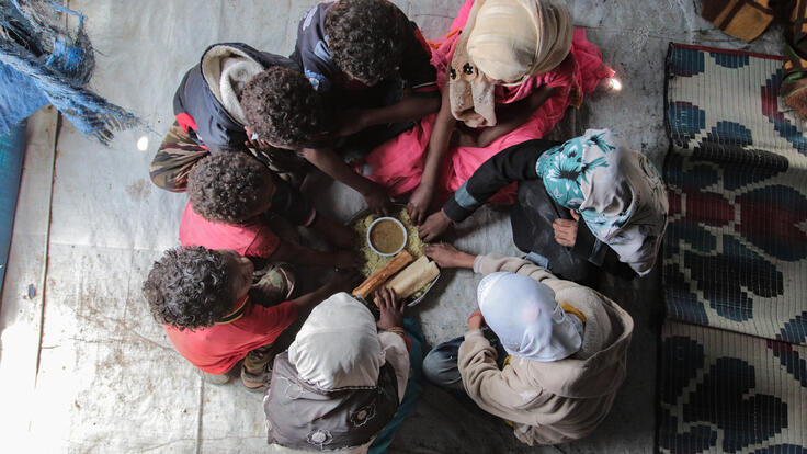 A family of 7 sit around a small plate of food.