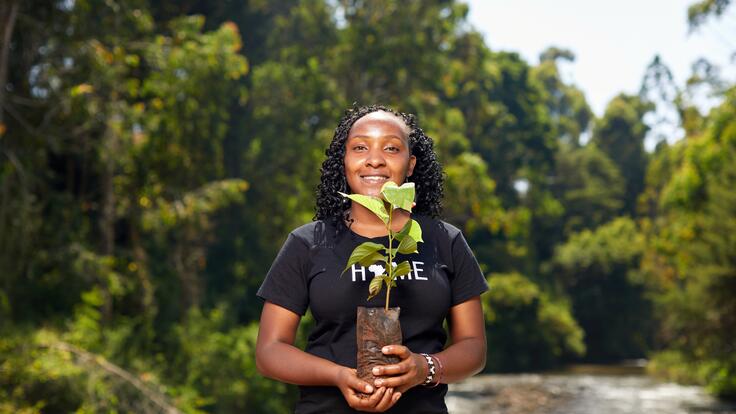  Elizabeth Wathuti looks at the camera and holds a vase with flowers outside in nature scenery 