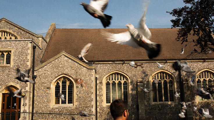 Maasom stands in front of a church in Andover as birds fly above his head.