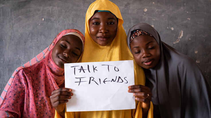three girls a the IRC's SAFE session hold up a sign that says 'Talk to friends'
