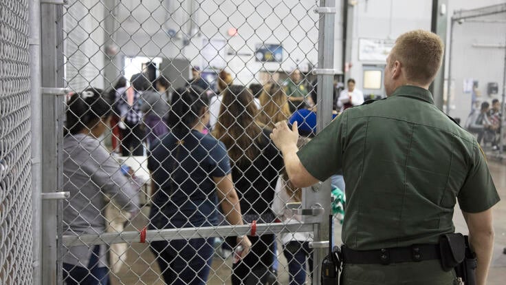 A U.S. border patrol officer at a gate as Central American families enter a detention facility after crossing the U.S.-Mexico border