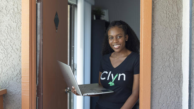 Diana Muturia, founder of the app Clyn, standing in a doorway and holding her laptop