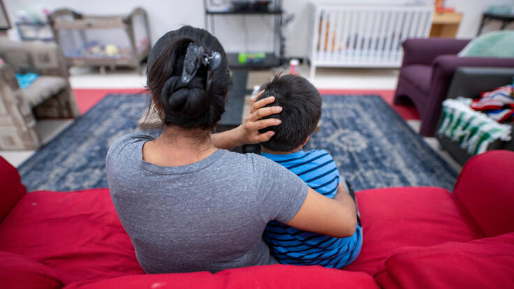 Angelina, an asylum seeker from Guatemala, sits on a red couch with her arms around her son at an IRC Welcome Center in Arizona. 