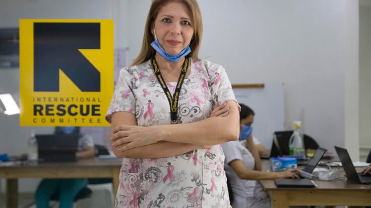 Dr. Edna Patricia Gomez stands in scrubs with her arms crossed. She has mask at her chin and there is an IRC logo behind her. 