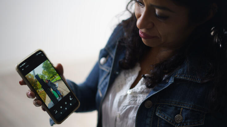 Rosa, wearing a jean jacket, holds an smart phone to show a photo of her daughter, Emily. 
