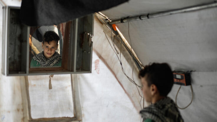 Omar, a 10-year-old Syrian boy, looks at himself in a mirror in his family's tent.