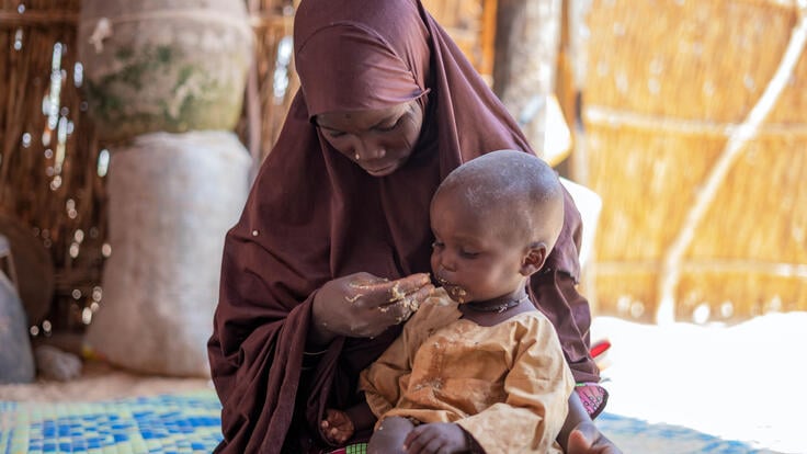 A mother in Niger sits on a mat feeding her baby, who is being monitored by the IRC for signs of malnutrition.