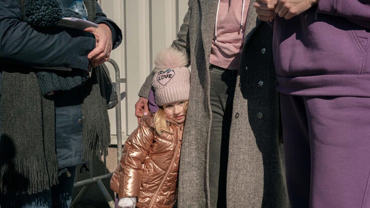 A young girl leans against her mother, all wearing winter clothes. 