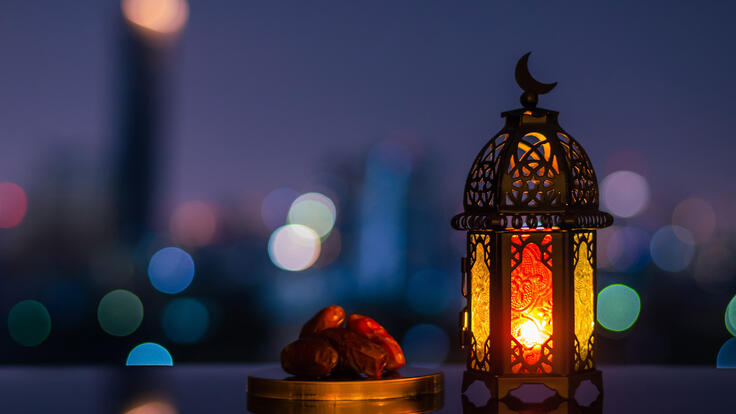 Lantern that have moon symbol on top and small plate of dates fruit with night sky and city bokeh light background for the Muslim feast of the holy month of Ramadan Kareem.