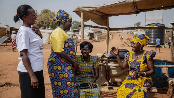 Foni Grace with other women in Togoleta. They are outside, two are sitting and two are standing, and they are laughing. 