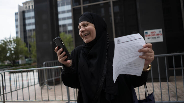 Maha smiles and holds her cell phone in one hand and an official-looking piece of paper in a another. She is standing outside the Jacob K. Javits Federal Building in lower Manhattan.
