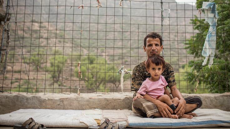 A man sits outside holding his child in his lap in a mountain village in Yemen where an IRC mobile health team provides care to families affected by conflict.