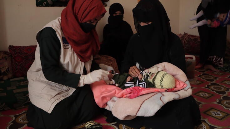 Dr. Bushra sits on a mat alongside her patient, whose newborn baby she is examining.