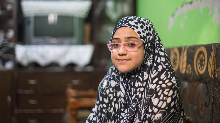 Salam sits on the ground and poses for the camera in her home