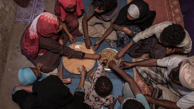 A family in Yemen is seated on the floor around plates of food for a meal.