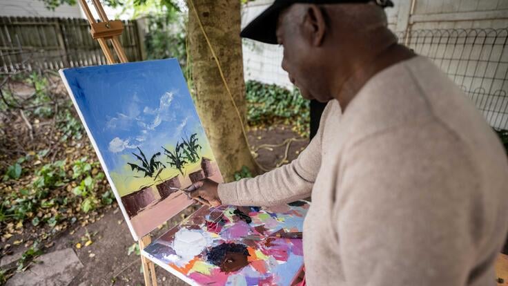 Muyambo Marcel Chishimba, an artist from Democratic Republic of Congo, paints a landscape with oil paints at an easel in his backyard in New Jersey