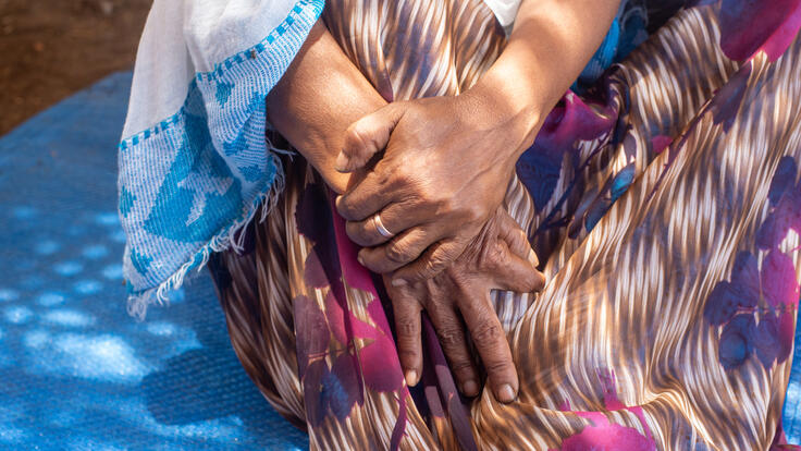 A closeup of 60-year-old Tigrayan refugee Berhan's hands, clasped on her lap.