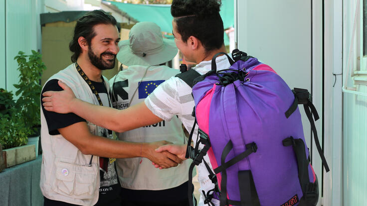 A teenage refugee boy and an IRC aid worker shake hands as the boy leaves a refugee camp in Greece