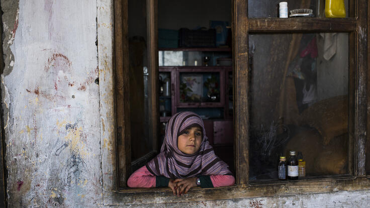 An Afghan girl looks out the window of her home