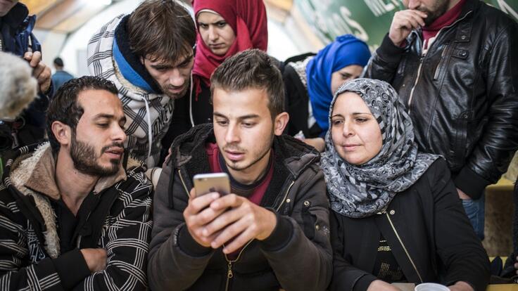 A group of refugees in Sid, Serbia, gather to access Refugee.Info on a mobile phone