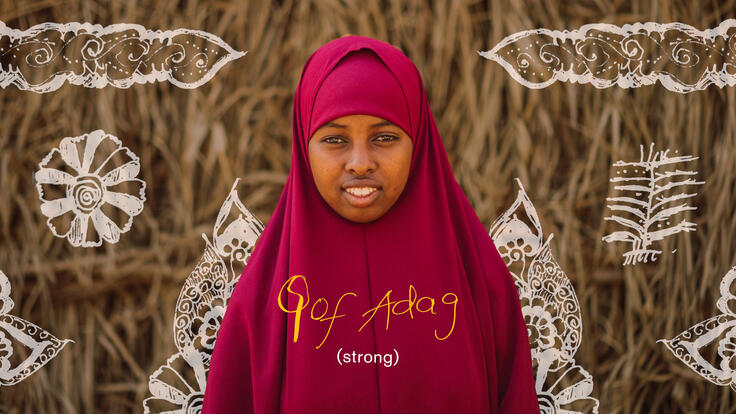 Smiling Suleykha with her doodle drawings in the background and her handwritten word to describe herself in Somali, translated as “Strong”