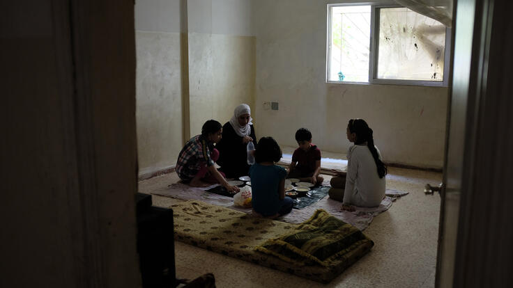 Amira and her four children sit together on the beige tiled floor in their apartment for a late lunch.
