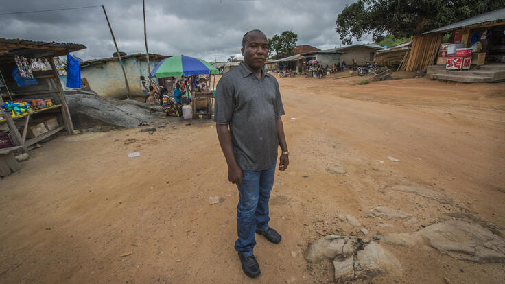 Alpha Tamba standing in a village plaza.