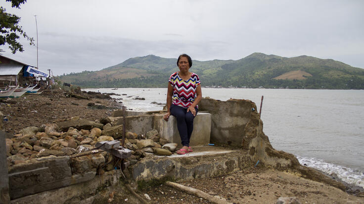 Erlima Azuelo standing in front of the ruins of her home.