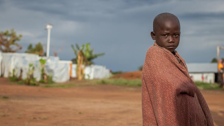 A child standing outside while wrapped in a blanket.