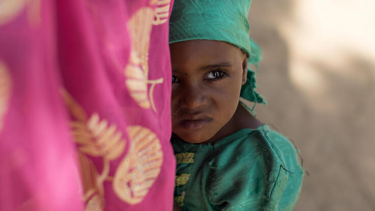 A little girl hiding behind her mother’s skirt.