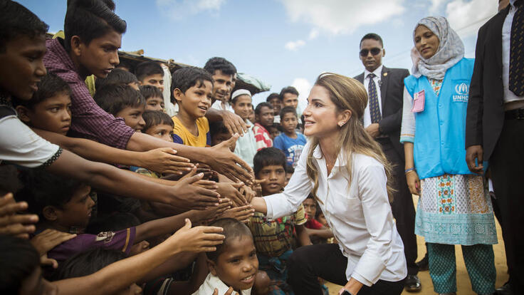 A group of children reaching out to shake Queen Rania's hand.