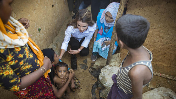 Queen Rania crouching and speaking to children surrounded by their family.