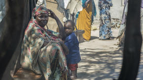 Displaced woman sits with a child outside a tent in Mogadishu