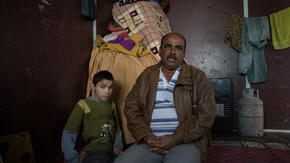 Abu Raed sits with his son Bashar, who is paralyzed, in their family's caravan at the Zaatari refugee camp in Jordan.