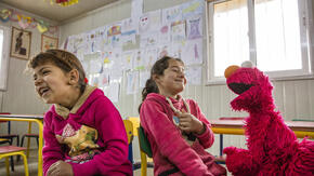 Elmo, the Sesame Street Muppet, makes two Syrian refugee girls laugh